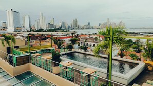 Une terrasse sur le toit dotée d’une piscine, de coins salon et offrant une vue sur les toits de la ville et le front de mer.