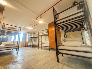 Ein Schlafraum im Schlafsaalstil mit Etagenbetten, Deckenventilator und einem fenster mit Vorhängen.