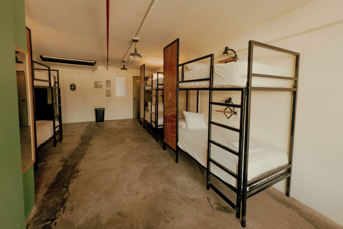 Quarto tipo dormitório com beliches, lixeira, porta e ventilador de teto.