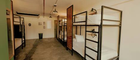 A dormitory room with bunk beds, a trash bin, a door, and a ceiling fan.