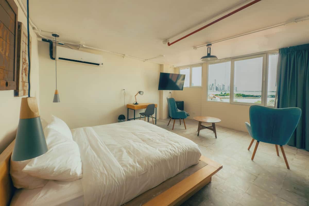 Quarto de hotel com cama, escrivaninha, cadeira, televisão e janela com vista para a cidade.