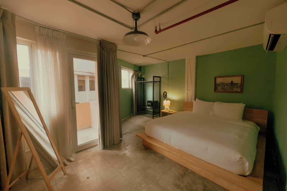 Quarto com cama grande, cabeceira de madeira, mesa de cabeceira com abajur, quadro na parede e porta deslizante para uma varanda.