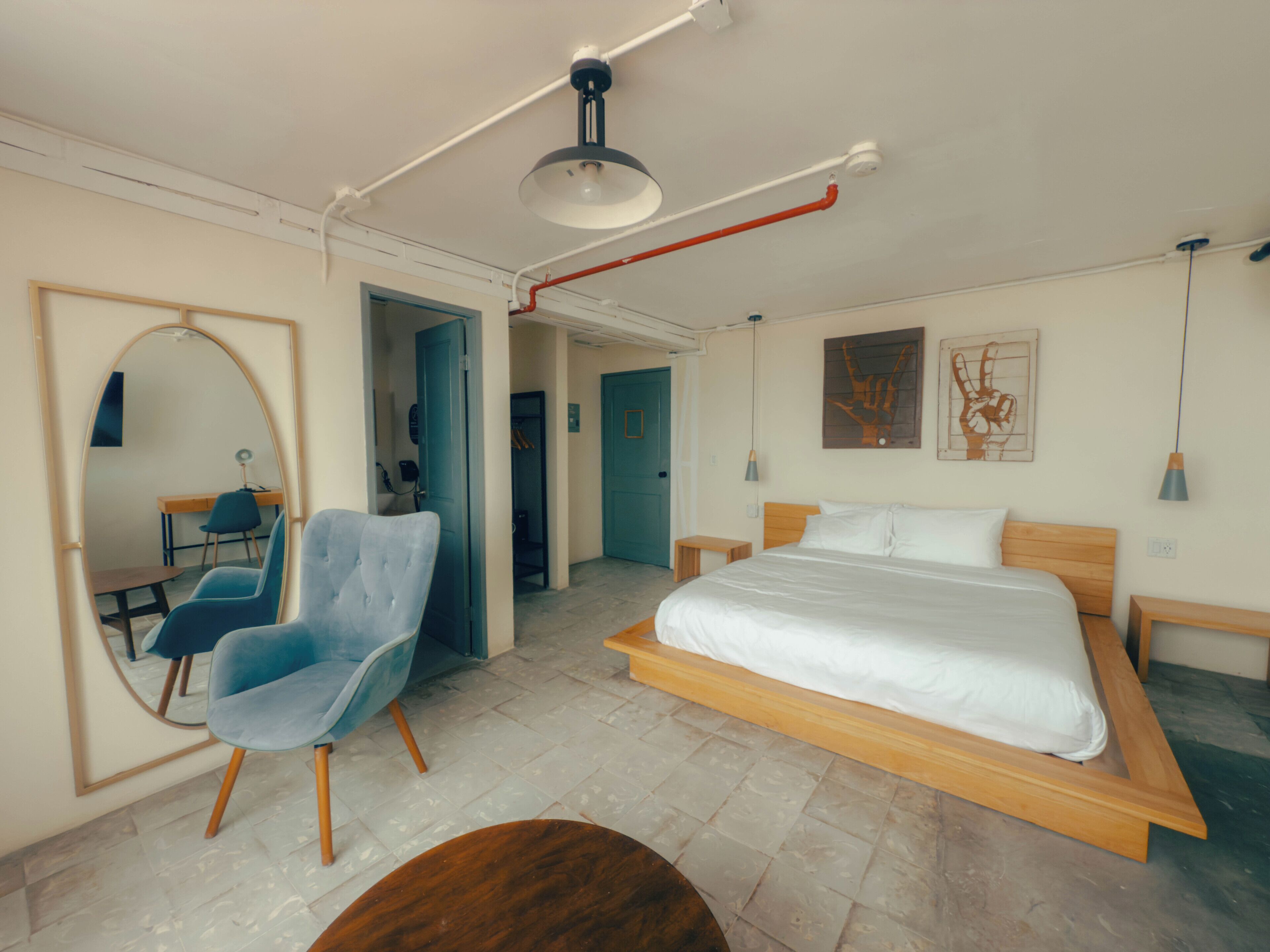 A modern bedroom with a large bed, a blue armchair, a wooden nightstand, and a mirror.