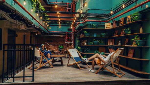 Un espace intérieur accueillant, aménagé avec des chaises et des tables en bois, entouré d’étagères où sont disposées des plantes et des livres.