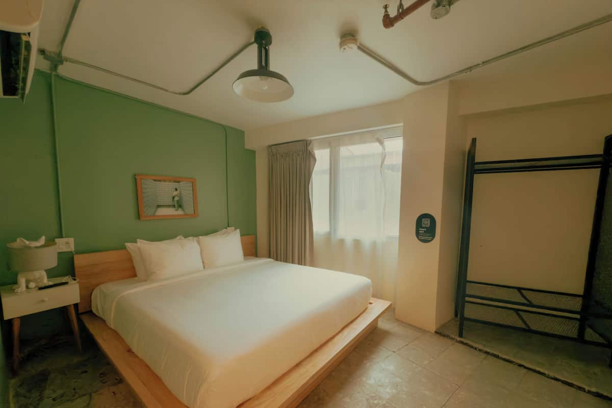 Quarto de hotel com cama, mesa de cabeceira, abajur, janela com cortinas e porta.