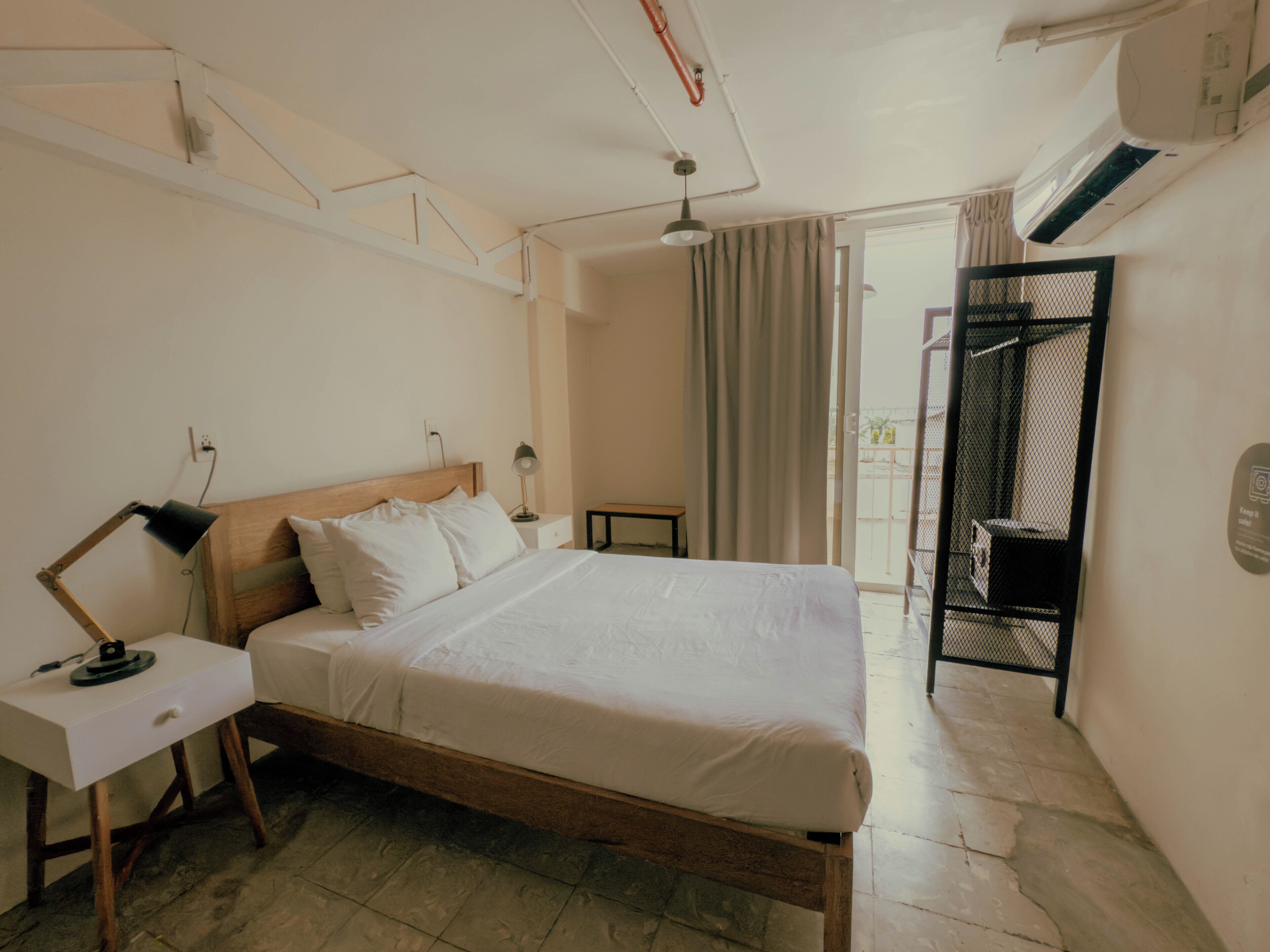A hotel room with a wooden bed, white bedding, a desk with a lamp, and a view of the outside through a sliding door.