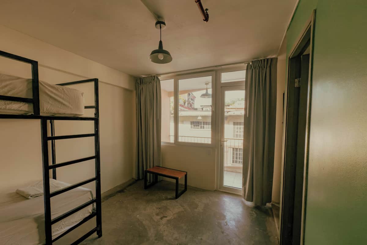 Um dormitório com beliches, um banco, uma janela e uma porta.