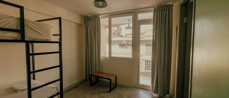 A dormitory room with bunk beds, a bench, a window, and a door.