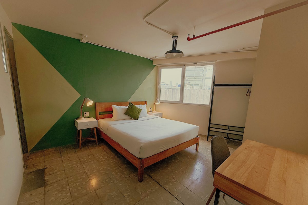 Um quarto com cama, mesas de cabeceira, uma janela e uma mesa de madeira.