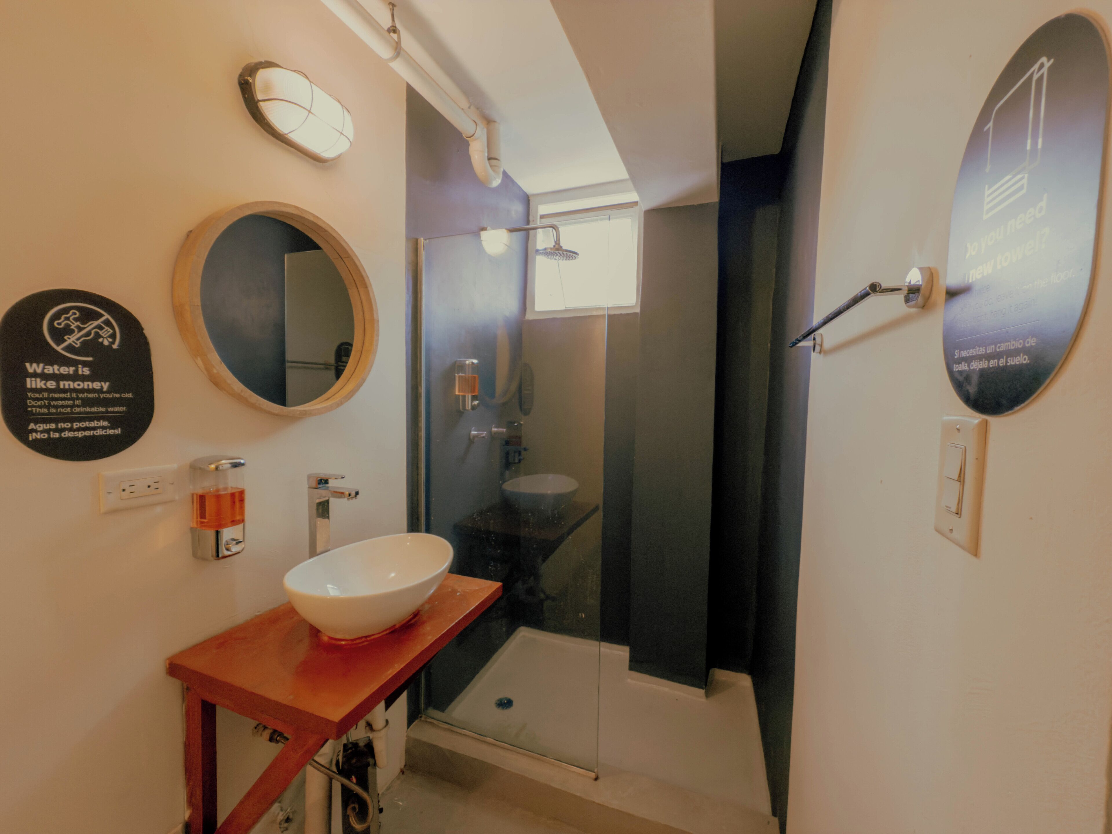 A bathroom with a round mirror, a white sink, and a glass shower enclosure.