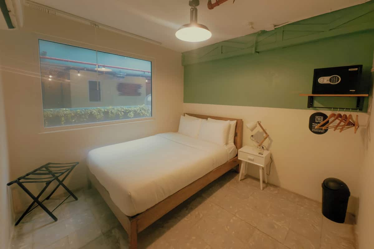 Quarto com cama, mesa de cabeceira, luminária pendente, janela e parede verde.