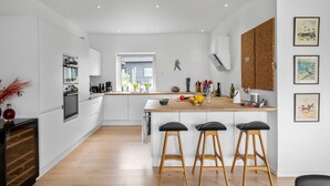 A modern kitchen with white cabinetry, a wooden countertop, and three black bar stools.