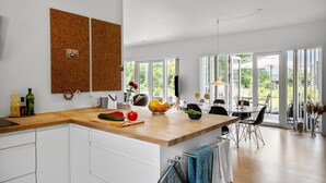 A modern kitchen with a wooden countertop, white cabinets, and a large window overlooking a garden.