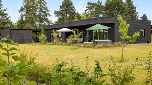 A modern two-story house with a covered patio area, a barbecue grill, and a small garden.