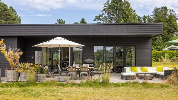 A modern house with a patio area featuring outdoor furniture, a grill, and a large umbrella.