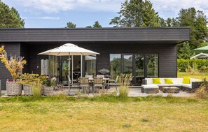 A modern house with a patio area featuring outdoor furniture, a grill, and a large umbrella.