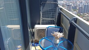 Un balcon avec une table et des chaises bleues, un barbecue en métal et une vue sur le paysage urbain.