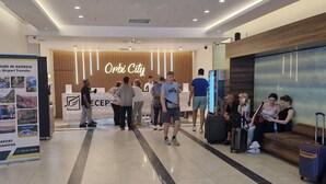 Un hall d’hôtel moderne avec un comptoir d’accueil, un espace salon et un panneau indiquant « Orbi City ».