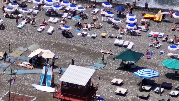 Une plage dotée de nombreux parasols et de chaises longues, d’une tour de surveillance pour les sauveteurs, et d’une côte rocheuse.