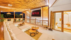 Ein stilvoller Wohnbereich mit einer großen Couch, einem kleinen runden Tisch und einem Fernseher, der 'NETFLIX' anzeigt.