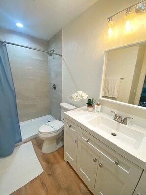 Een moderne badkamer met een douche, toilet, wastafel en een grote spiegel.