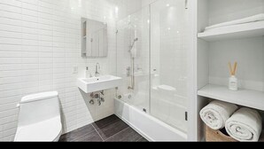 A modern bathroom with white fixtures, a glass shower enclosure, and neatly arranged towels. - Spacious, luxury, central 3-bed, toilet, laundry apartment with dishwasher (New York)