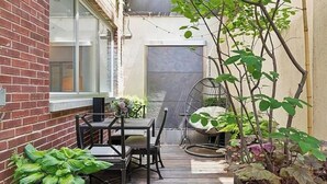 A narrow outdoor patio with a wooden table and chairs, surrounded by potted plants and a hanging chair. - Spacious, luxury, central 3-bed, toilet, laundry apartment with dishwasher (New York)