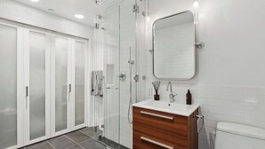 A modern bathroom with a glass shower enclosure, a wooden vanity, and a white toilet. - Spacious, luxury, central 3-bed, toilet, laundry apartment with dishwasher (New York)