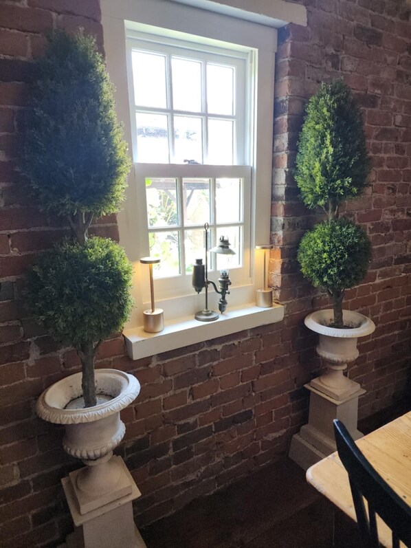 A brick wall with a window, two potted trees, a table, and a chair. - Varcoe House Award-Winning Historic Home | Sleeps 8 | Weddings & Events Friendly (Newcastle)