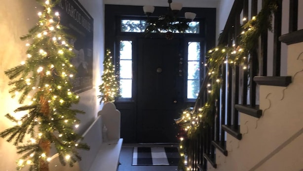Un pasillo con un árbol de Navidad y guirnalda, una puerta negra y un felpudo a cuadros en la entrada.