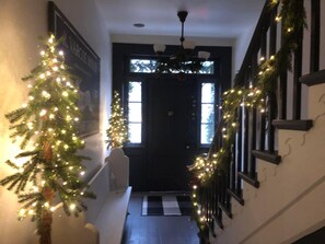 A hallway with a Christmas tree and garland, a black door, and a checkered mat at the entrance. - Varcoe House Award-Winning Historic Home | Sleeps 8 | Weddings & Events Friendly (Newcastle)