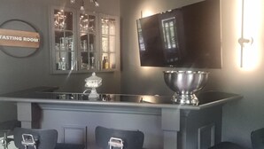 Un moderno salón de degustación con zona de bar, taburetes, un bol grande de metal y un televisor en la pared.