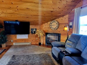 A cozy living room with a wooden ceiling, a television, a fireplace, and a sofa.