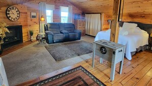 Interior de una cabaña de troncos con chimenea, un sofá, una cama y un ventilador de techo.