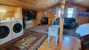 Interior acogedor de una cabaña con pisos de madera, chimenea, televisor, reloj y sofá.