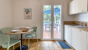 Una cocina compacta con comedor, una mesa pequeña con sillas y vista a una terraza exterior por una puerta de vidrio.