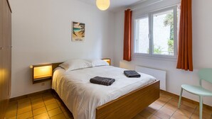 Un dormitorio con cama de madera, lámpara de noche, ventana con cortinas e imagen colgada en la pared.