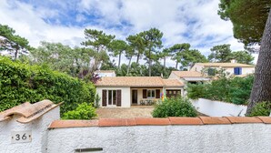 Una villa con techo de tejas, un patio con mobiliario exterior y una pared blanca con placa de número.