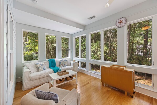 A spacious living room with large windows, a white sofa, a wooden coffee table, and a wooden cabinet.