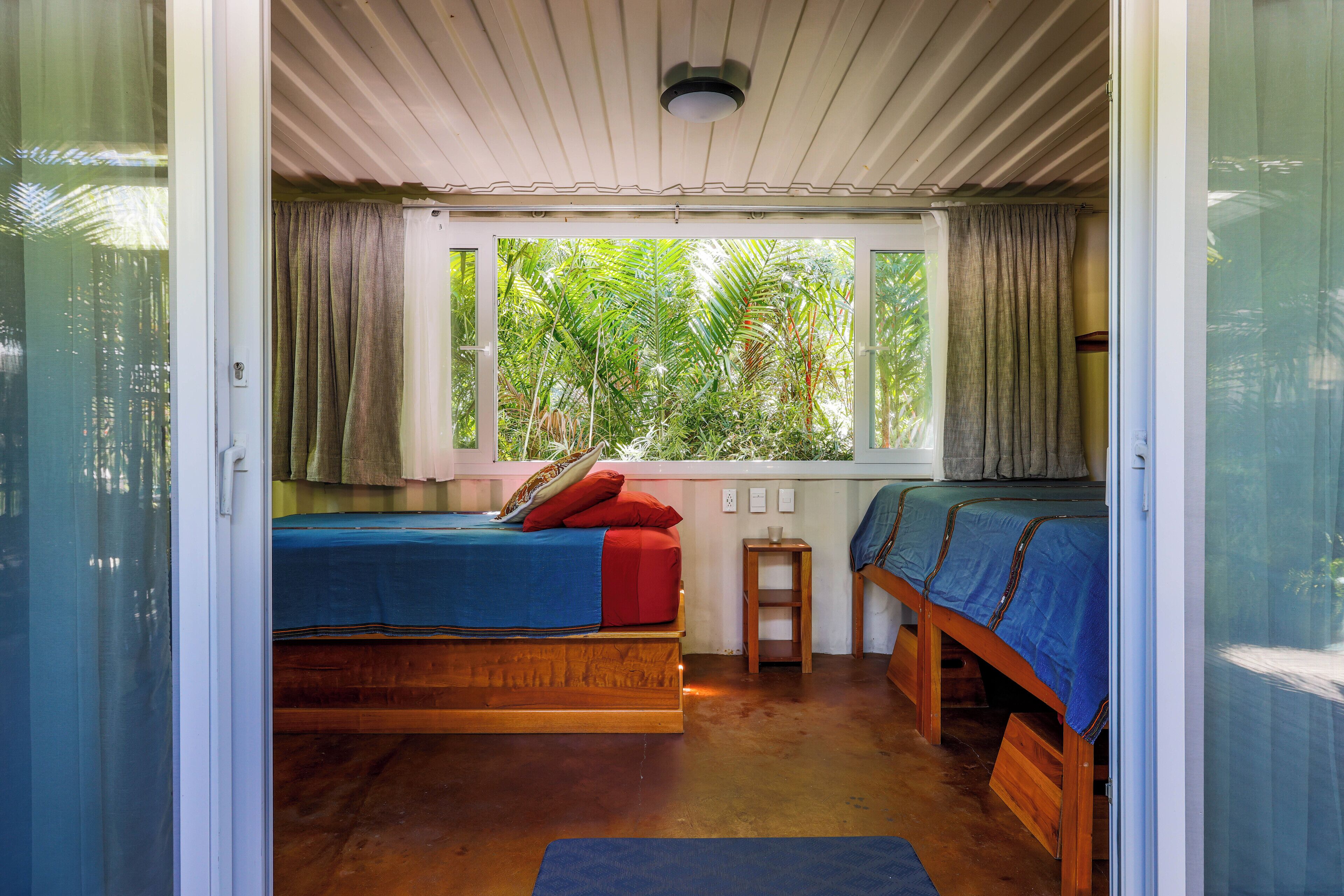 A room with two wooden beds, a small table, and a window with curtains.