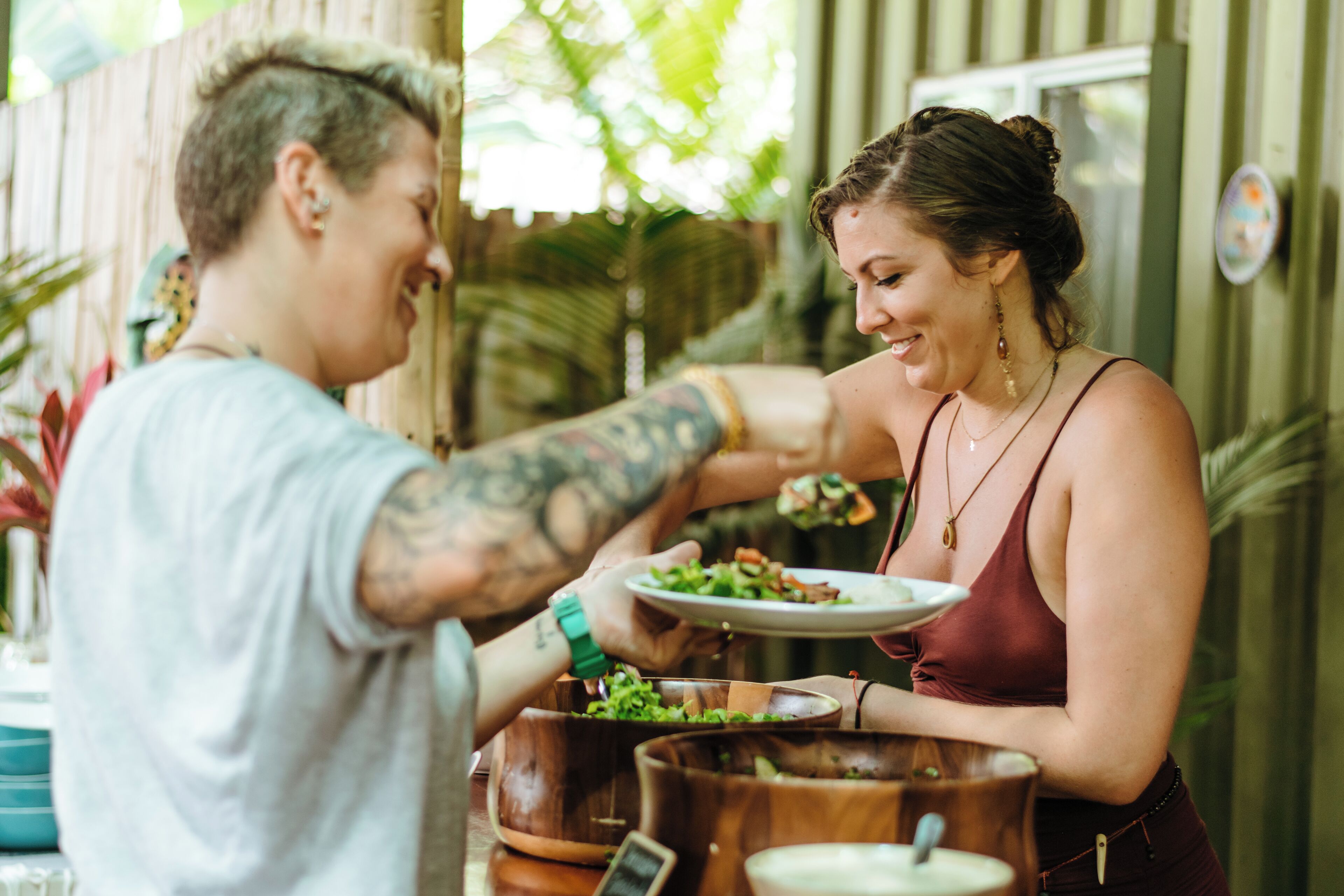 A person serving food to another person at a table with a wooden bowl and a plate.