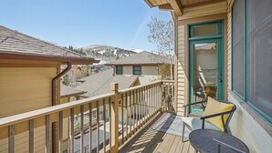 A wooden deck with a view of a mountain, a door with a green frame, and a chair with a yellow cushion.