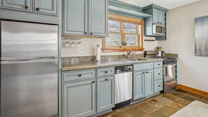 A kitchen with light blue cabinets, a stainless steel refrigerator, a microwave, and a stove.