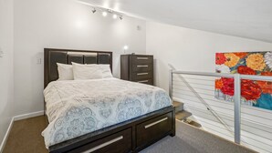 Un dormitorio con cama, mesita de noche, cómoda y un cuadro en la pared.