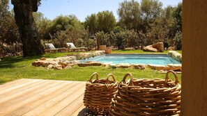 Un área de piscina con sillas de descanso, una terraza de madera y un borde de piedra.