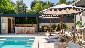 Un espace piscine avec un bar, des sièges extérieurs et des parasols.