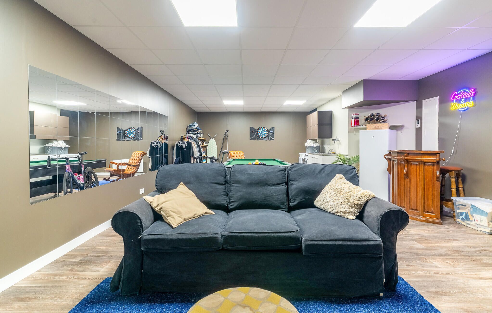 A room with a black sofa, a dartboard, and a billiards table.