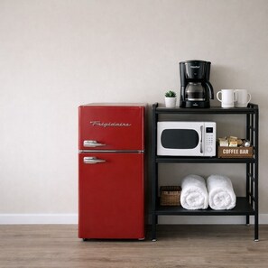 Un frigorifero Frigidaire rosso, un forno a microonde bianco, una macchina da caffè e uno scaffale con asciugamani e una piccola area dedicata al caffè.