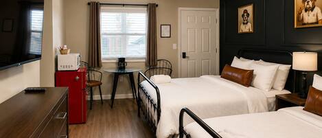 A hotel room with two beds, a desk, a TV, and a window with curtains.