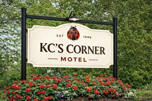 A sign for KC's Corner Motel with a ladybug logo, established in 1990, surrounded by colorful flowers. - Comfy & Pet Friendly Stay Near Cooperstown (East Springfield)